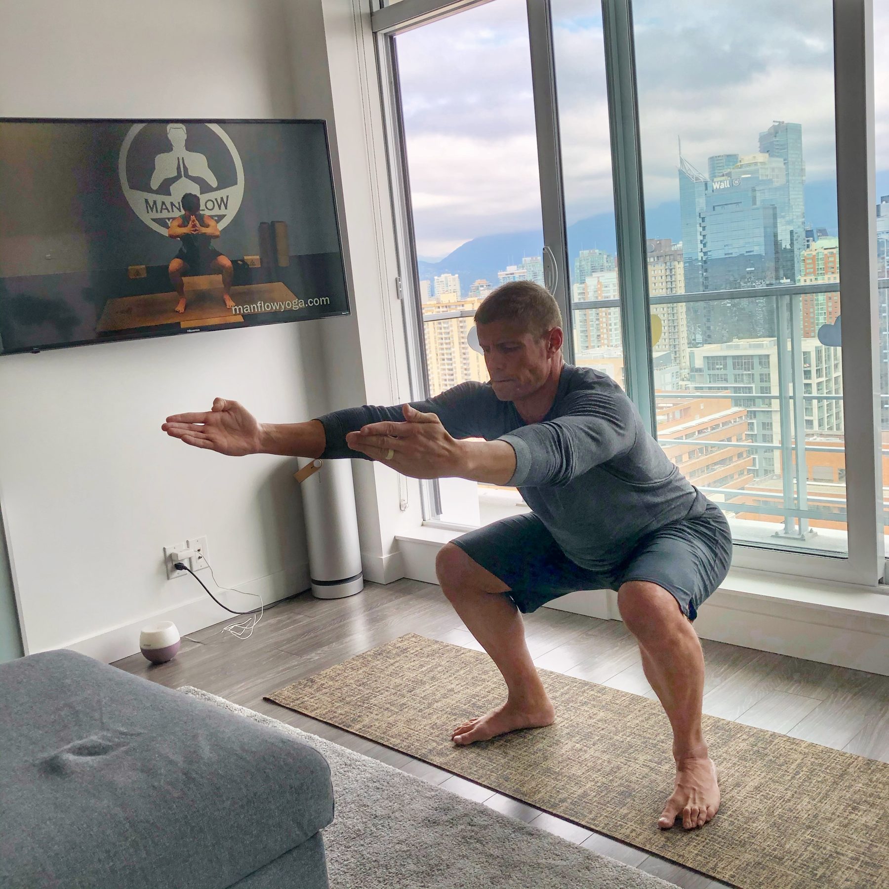 Dai Manuel holding a deep squat on a mat at home by a window